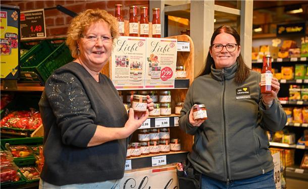 Zwei Frauen, die Gläser mit Chutney-Füllung präsentieren. Hinter ihnen steht ein Verkaufsregal.