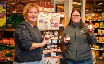 Zwei Frauen, die Gläser mit Chutney-Füllung präsentieren. Hinter ihnen steht ein Verkaufsregal.