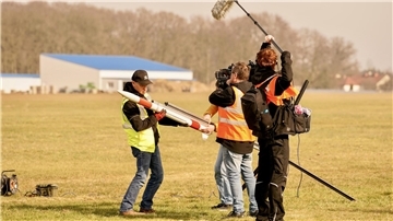 Ein Mann hat eine Rakete in der Hand, dabei wird er von einem Filmteam gefilmt.