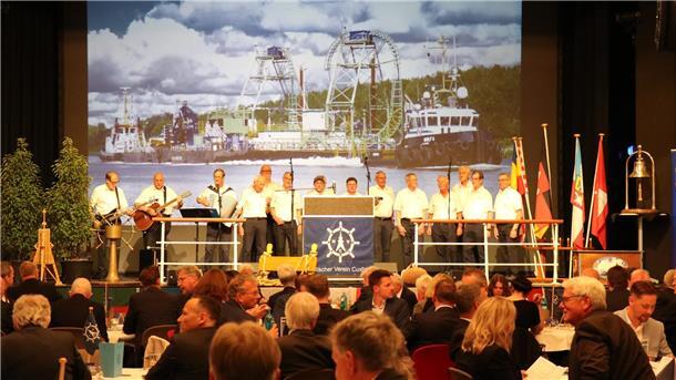 Ein Shanty-Chor steht auf einer Bühne. Davor sitzt das Publikum