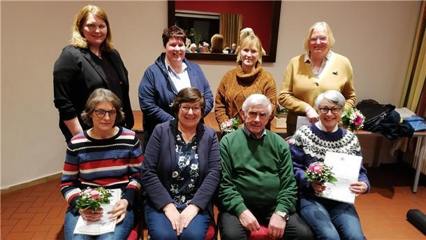 DRK Lunestedt freut sich über positive Entwicklung des Jugendrotkreuzes Eine Gruppe von acht Personen, überwiegend Frauen, posiert für ein Foto in einem Innenraum mit einer schlichten Wand und einem Spiegel im Hintergrund. Einige halten Blumensträuße und Urkunden in den Händen.