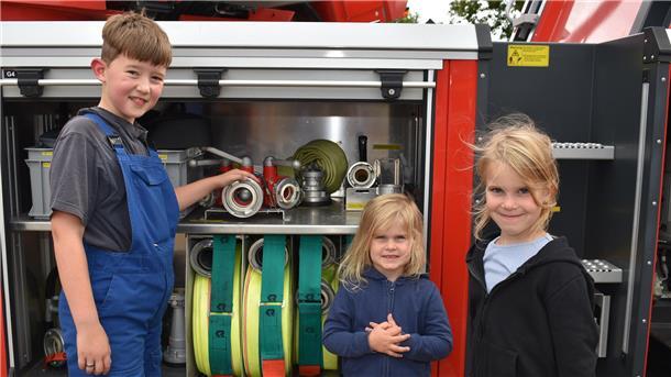 Der gerade von der Kinder- in die Jugendfeuerwehr gewechselte zehn Jahre alte Max Engling zeigt zwei jungen Besucherinnen die Ausrüstung eines Feuerwehrautos.