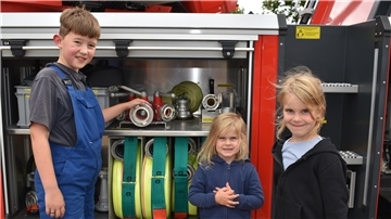 Der gerade von der Kinder- in die Jugendfeuerwehr gewechselte zehn Jahre alte Max Engling zeigt zwei jungen Besucherinnen die Ausrüstung eines Feuerwehrautos.