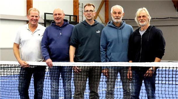 Fünf Männer stehen hinter einem Tennisnetz und lächeln in die Kamera.