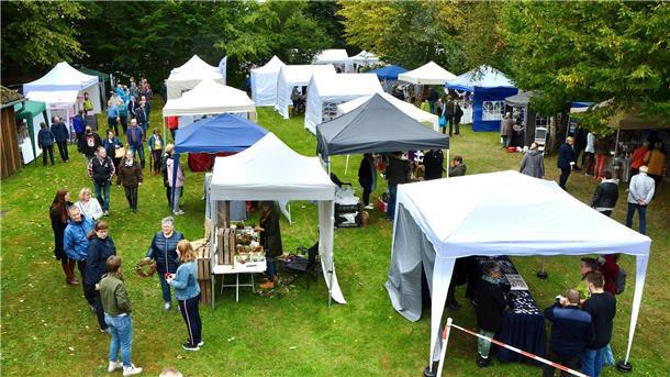 Zum Jubiläum gibt es einen Drechsler beim Kunsthandwerkermarkt in Hesedorf Auf einer Wiese stehen überdachte Stände. Besucher stehen im Freien