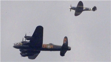 Ein Lancaster-Bomber wird von einem Jagdflugzeug begleitet.