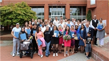 Große Gruppe lächelnder Menschen mit Blumen und Urkunden 