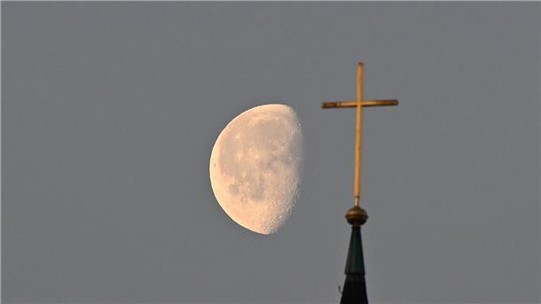 Kirchenbindung und die Religiosität gehen zurück Der Mond im Morgenlicht hinter einem Kreuz auf einem Kirchturm.