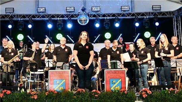 Männer und Frauen in schwarzen Poloshirts stehen auf einer beleuchteten Bühne in einem Festzelt