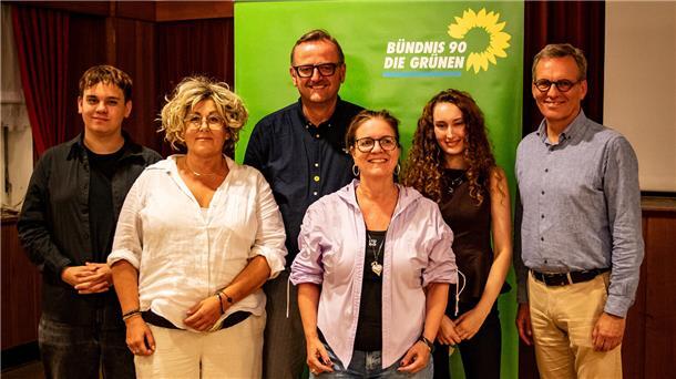 Ein Gruppenfoto mit mehreren Menschen vor einem Banner, auf dem grünen Bündnis 90/Die Grünen steht. 