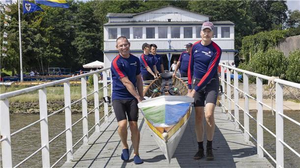 Ruderer tragen bei der Regatta des Ruderclubs Nordenham ein Boot über den Steg. 