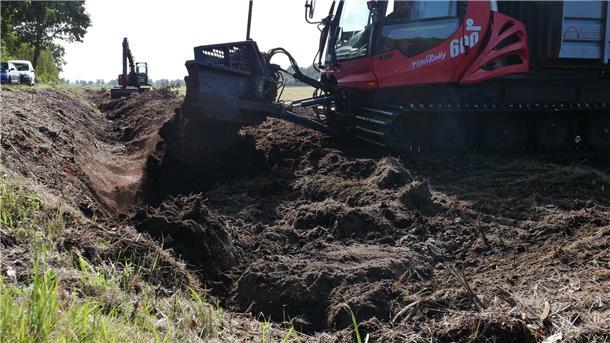 Ein Pistenbully verfüllt einen Graben mit Torf.