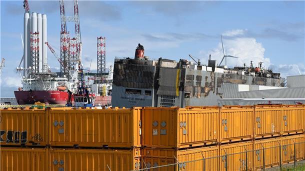 Nach Großfeuer: Beschädigter Frachter im sicheren Hafen Der schwer beschädigte Autofrachter „Fremantle Highway„ wird durch gelbe Container abgeschirmt.