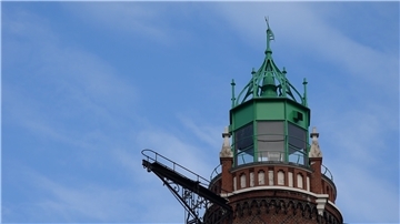 Die grüne Haube eines Leuchtturms vor blauem Himmel.