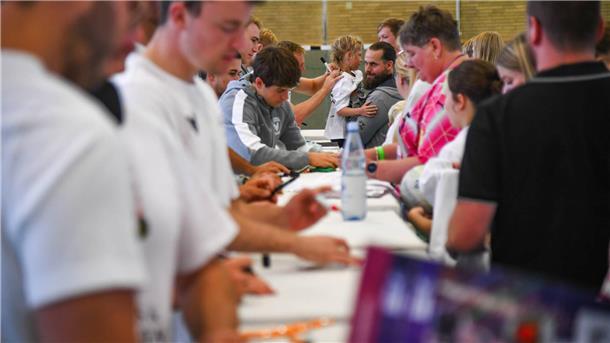 Menschen in einer Sporthalle geben Autogramme. 