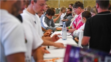 Menschen in einer Sporthalle geben Autogramme. 