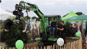 Garten- und Landschaftsbauer machen Gärten fit für den Klimawandel Ein Mann lenkt einen grünen Bagger und ein anderer Mann erklärt ihm, was er machen soll.