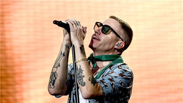 Sänger Macklemore singt bei einem Auftritt vor einer beleuchteten LED-Wand.