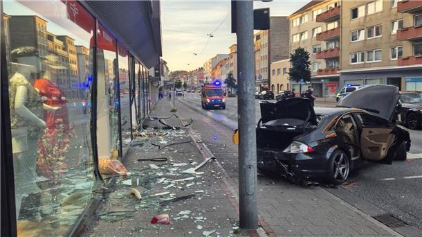 Bremerhaven: 22-Jähriger rast mit Wagen in Schaufenster Glasscherben von einem Schaufenster liegen auf einem Fußweg. Daneben steht ein stark beschädigter schwarzer Wagen.
