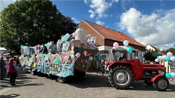 Festlich geschmückter Umzugswagen mit bunten Meeresmotiven und Ballons beim Wremer Ernteumzug. Ein roter Traktor zieht den Wagen durch eine mit Zuschauern gesäumte Straße bei Sonnenschein.