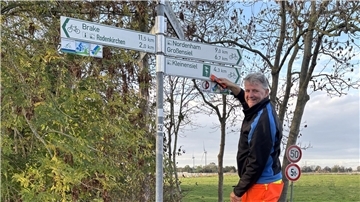 Der Radwegewart Holger Jacobs steht auf einer Leiter und repariert ein Radwegeschild. 