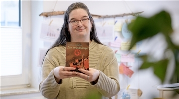 Eine Frau mit braunen Haaren zeigt das Buch "Der Windsänger" in die Kamera.