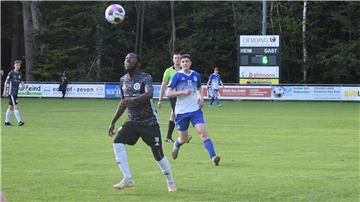 Zwei Männer in einem schwarzen und einem blauweißen Trikot laufen hinter einem Ball her.