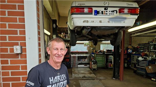 Ein Mann vor einem Auto, dass auf einer Hebebühne hochgefahren ist.