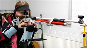 Eine Frau blickt durch das Zielfernrohr eines Sportgewehrs.