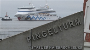 Das Schiff "AIDAaura" fährt im Bildhintergrund auf dem Wasser.