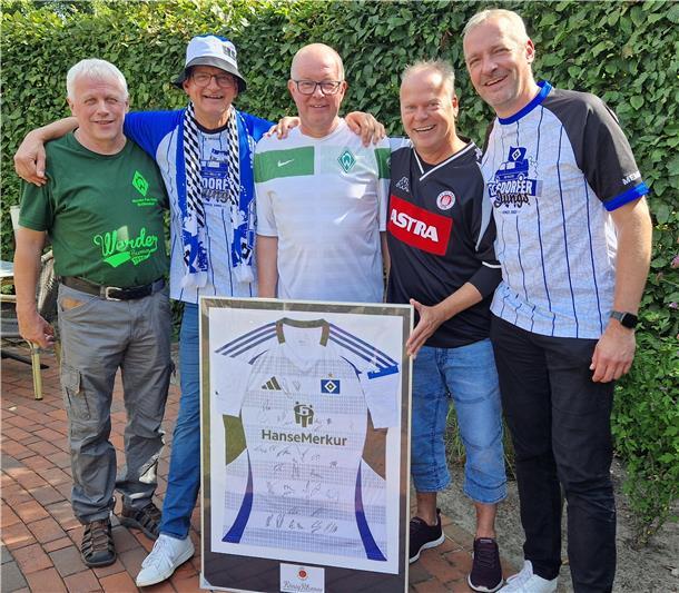 Top, die Wette gilt: Traditionelle Fußballwetten erleben ein Comeback Fünf Männer stehen nebeneinander, halten ein gerahmtes HSV-Trikot fest und lächeln in die Kamera.