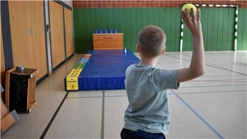 Ein Junge ist von hinten zu sehen und will mit einem Ball werfen.