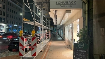 Blick auf einen Fußweg und einen Radweg, auf dem ein Baugerüst steht. Oben im Bild ist der Schriftzug "Schuback Parfümerie" zu sehen. Links fahren Autos eine Straße entlang.