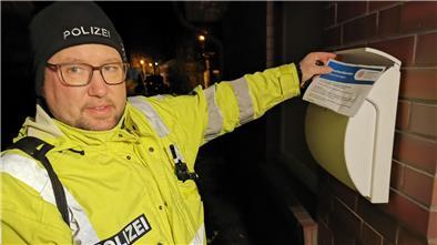 Ein Polizist steckt ein ausgefülltes Formular in einen Briefkasten.