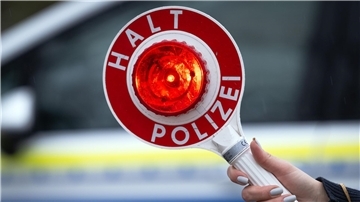 Eine Polizistin hält während einer Verkehrskontrolle eine Polizeikelle mit der Aufschrift „Halt Polizei“. 