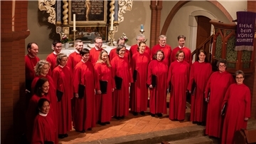 Menschen in roten Chorgewändern stehen vor einem Altar. 