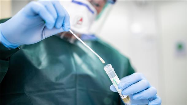 Canan Emcan, Stationsleiterin auf der Infektionsstation der Uniklinik Essen, steht in Schutzkleidung und mit einer Atemmaske in einer Schleuse und hält ein Abstrichröhrchen in den Händen.