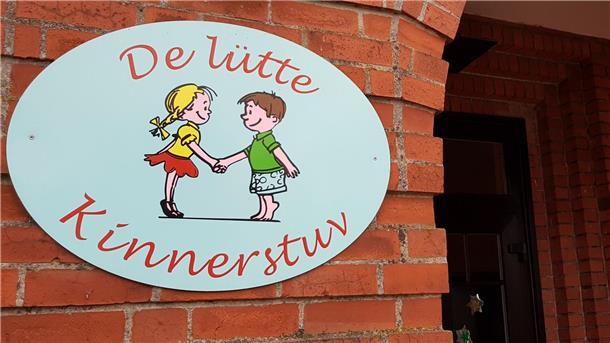 Schild mit Mädchen und Junge an einer Backsteinwand. Darauf geschrieben steht "De lütte Kinnerstuv".