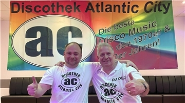 Zwei Männer strecken vor einem Banner mit der Aufschrift „Discothek Atlantic City" den Daumen in die Luft. Die DJs Markus Becker und Olli Hübler laden zur AC-Party ein. 