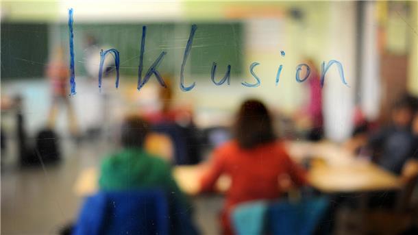 Schüler sitzen in einem Klassenraum unter einem Schriftzug "Inklusion", Aufnahme durch eine beschriebene Glasscheibe hindurch