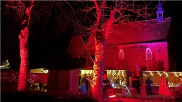 Eckwarder Kirche in buntes Licht getaucht, davor die Buden eines kleinen Weihnachtsmarktes. 