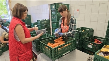Zwei Frauen sortieren Obst und Gemüse in einem Raum, der voller grüner Kisten steht