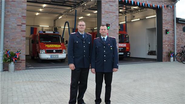 2 Männer in Uniform vor Haus mit Feuerwehrfahrzeugen