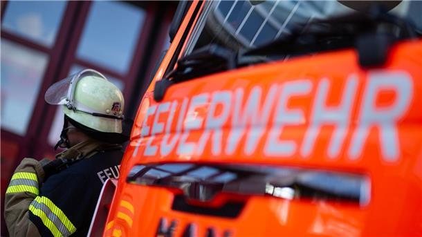 Eine Einsatzkraft der Feuerwehr steht neben einem Einsatzfahrzeug der Feuerwehr.