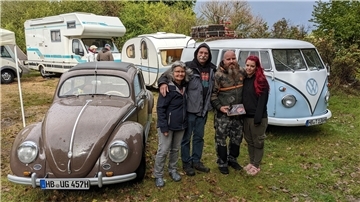 Vier Menschen stehen neben einem VW-Käfer.