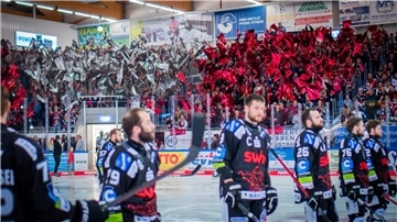 Eishockeyspieler stehen auf dem Eis. Die Fans auf der Tribüne halten rote und weiße Fahnen hoch.