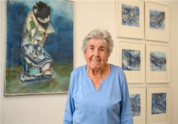 Eine Frau steht vor einer mit Bildern behängten Wand.