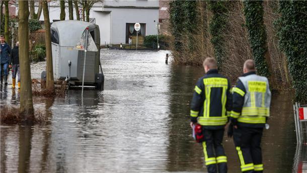 Feuerwehrleute stehen an einer überfluteten Wohnstraße