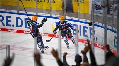 Fans bejubeln zwei Eishockeyspieler auf dem Eis, die sich über ein Tor freuen. Es sind die Fischtown Pinguins aus Bremerhaven.