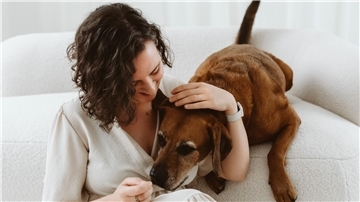 Eine Dame sitzt mit ihrem Hund an einem Sofa. 